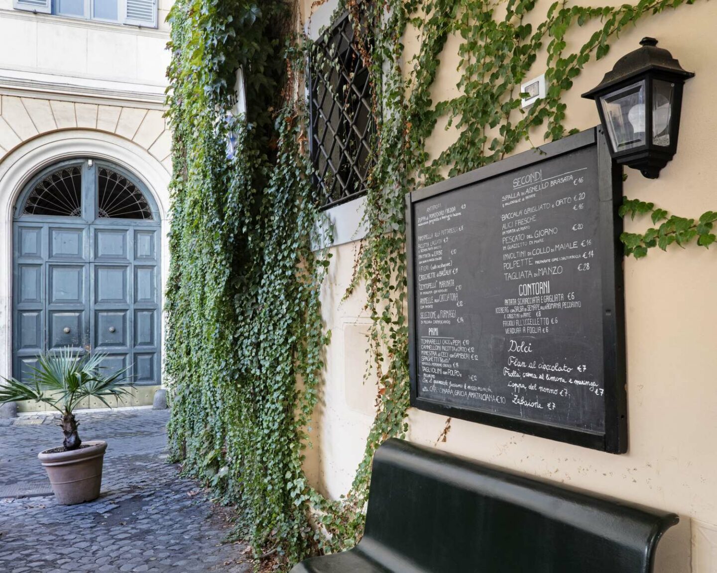 dehors ristorante con lavagna nera con menu e edera sul muro