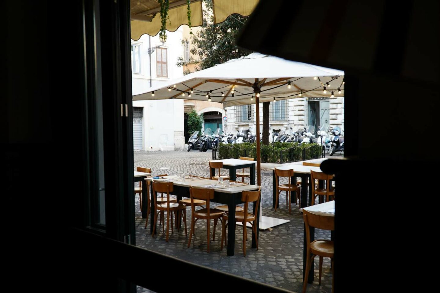 sala esterna vista dall'interno: tavoli di legno apparecchiati, gazebo con tenda bianca e lucine accese